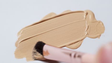 Brushing-a-smudge-of-nude-colored-foundation,-using-a-brush-applicator-on-a-clean,-white-paper-board