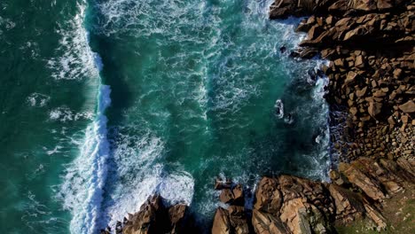Green-Ocean-Waves-Along-Rocky-Cornish-Coastline,-Aerial-Top-Down-Panning-Shot