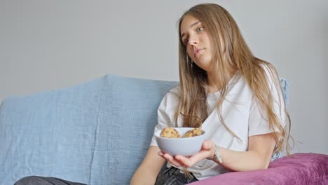 Attractive-Woman-at-Home-Using-Remote-Control-for-Television-While-Holding-a-Bowl-of-Cookies