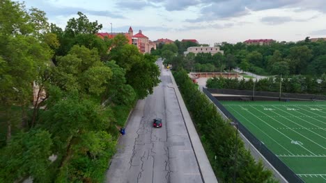 Aerial-tracking-shot-of-sedan-car-driving-on-college-campus-at-sunset