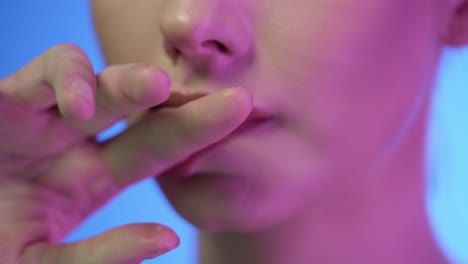 Extreme-close-up-of-young-beautiful-woman-while-she-seductively-strokes-finger-over-her-red-full-lips-with-purple-contrast-on-her-face-in-slow-motion