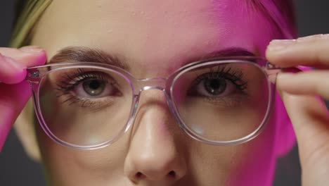 Close-up-of-a-young-pretty-beautiful-woman-while-looking-neutrally-into-the-camera-and-taking-on-her-glasses-with-purple-light-in-her-face-in-slow-motion