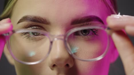 Close-up-of-a-young-pretty-woman-wearing-glasses-while-looking-neutrally-into-the-camera-and-taking-off-her-glasses-with-purple-light-in-her-face-in-slow-motion