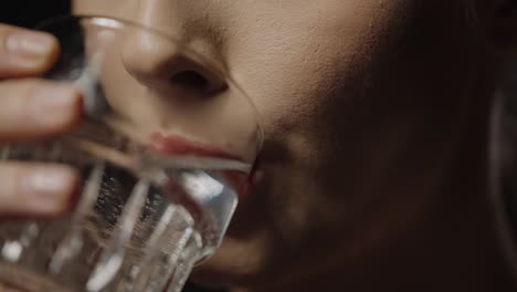 Close-up-shot-of-a-beautiful-woman-with-full-beautiful-lips-drinking-a-glass-of-water-to-quench-her-thirst-against-black-background-in-slow-motion