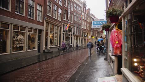 Wide-view-of-Amsterdam-shopping-street-with-stores-and-pride-flags-on-facade-of-bar