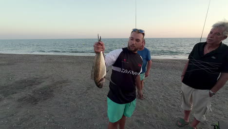 Hombre-Sujetando-Un-Pez-Vivo-Capturado-Por-Un-Pescador-Pescando-A-Lo-Largo-De-Una-Playa-En-España
