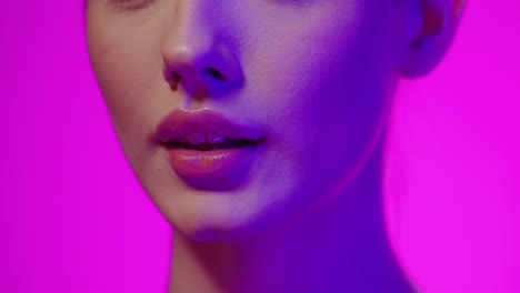 Extreme-close-up-of-a-young-woman-holding-her-finger-to-her-lips-to-symbolize-silence-or-being-quiet-in-front-of-purple-background-in-slow-motion