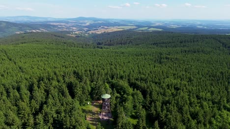 Drone-view-as-it-flies-over-the-trees-and-rotates-above-the-lookout-tower-on-the-mountains-with-the-valley-in-the-background