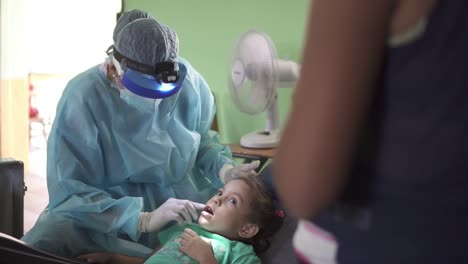 Eine-Zahnärztin-Untersucht-Während-Einer-Medizinischen-Brigade-In-Einer-Improvisierten-Klinik-In-Einer-Armen-Gemeinschaftsschule-Den-Mund-Eines-Kleinen-Mädchens