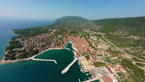 High-angle-drone-establishing-view-of-Cres-Island-Croatia-at-midday,-sprawling-village-homes,-cinematic-dive-down-to-harbor
