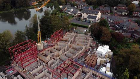 Aerial-view-looking-down-over-crane-care-home-development-site-in-rural-British-village-next-to-fishing-lake