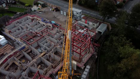 Aerial-view-descending-above-crane-on-care-home-construction-development-in-rural-British-village-next-to-fishing-lake