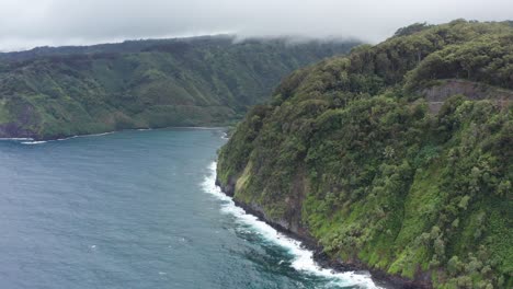 Aerial-close-up-shot-flying-over-the-steep-jungle-cliffs-along-the-rugged-coastline-of-the-Road-to-Hana-in-Maui,-Hawai'i