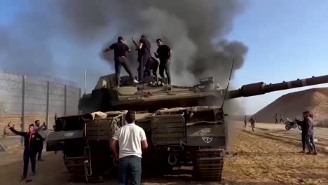 Palestinos-En-Un-Tanque-Militar-Israelí-Destruido-En-La-Valla-De-La-Franja-De-Gaza,-Operación-De-Inundación-De-Al-Aqsa-Por-Parte-De-Hamas-10-07-2023