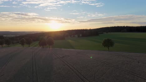 Drone-view-as-it-flies-over-the-countryside-moving-away-from-the-sunset-while-rotating