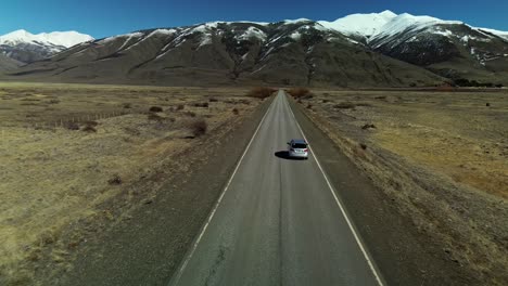 Drone-forward-flight-following-silver-car-on-scenic-road-towards-Patagonian-Mountains-during-summer-day,-Argentina