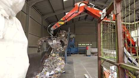 Large-tractor-moves-paper-waste-from-bin-to-conveyor-belt-at-recycling-plant