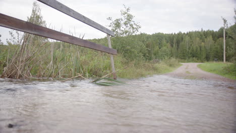 River-overflowing-at-gravel-road-due-to-rainwater-runoff,-climate-change