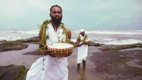 Nahaufnahme-Von-Zwei-Afrikanischen-GA-Traditionalisten,-Die-Kalebasse-Halten-Und-Rituale-Und-Trankopfer-Auf-Felsen-Am-Meer-Durchführen