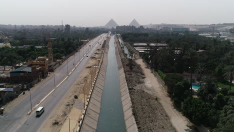 Aerial-Shot-Track-out-and-rising-up-for-The-Pyramids-of-Egypt-in-Giza-in-the-background-of-a-branch-of-the-River-Nile-in-the-foreground-Maryotya-branch-and-birds-are-passing-in-the-front