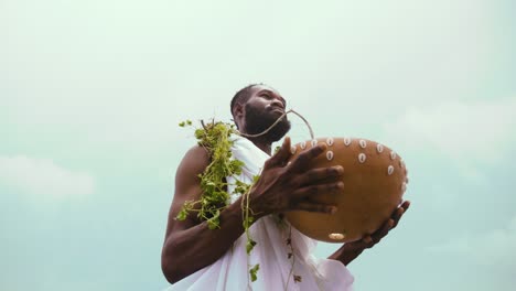 Zeitlupen--Und-Tiefwinkelaufnahme-Eines-Afrikanischen-GA-Traditionalisten,-Der-Während-Der-Trankopferung-Eine-Kalebasse-Mit-Gras-Am-Hals-Hält-Und-Weißes-Tuch-Trägt