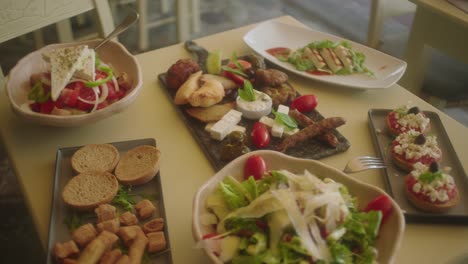Wide-shot-of-assorted-greek-food-on-table-including-salads,-cheese-and-bread