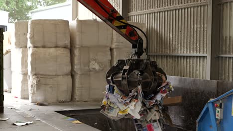 Tractor-claw-moving-paper-from-container-to-conveyor-belt-at-recycling-center