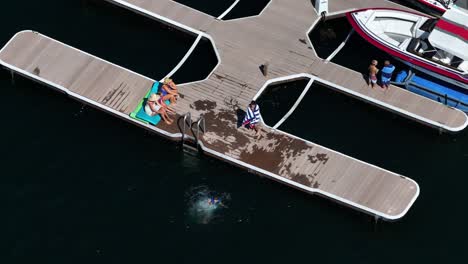 little-kid-jumping-into-the-water-off-of-a-boat-dock-family-enjoying-a-relaxing-time-on-the-boat-dock-in-lake-arrowhead-california-AERIAL-TELEPHOTO-STATIC