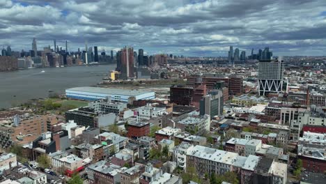 Slow-forward-flight-over-american-neighborhood-beside-river-and-skyline-during-cloudy-day-in-background---New-York-City,-USA