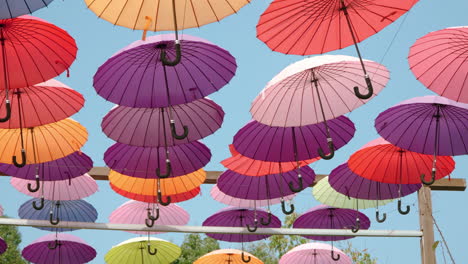 Wandern-Unter-Bunten-Regenschirmen,-Die-Oben-In-Der-Luft-Vor-Blauem-Himmel-Hängen,-Auf-Der-Kräuterinsel-In-Pocheon-–-Künstlerische-Gehwegdekoration