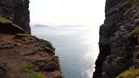 Static-shot-of-sun-reflection-on-Atlantic-Ocean-between-rocky-mountain-cliffs-on-Vagar-Island,-Faroe-Islands