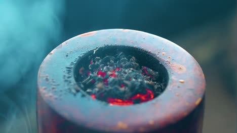 extreme-close-up-of-tobacco-burning-inside-a-pipe-that-has-been-damaged-by-the-fire-being-always-in-close-distance-leaves-producing-thick-clouds-of-smoke-that-is-blue-colour-shade-and-ash-is-visible