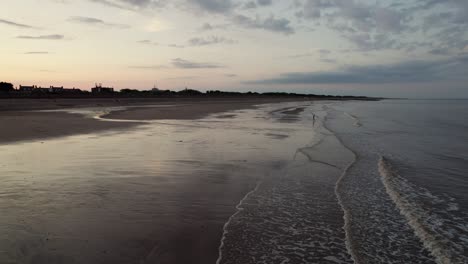 Von-Oben-Aufgenommen,-Gibt-Es-Luftaufnahmen-Eines-Wunderschönen-Strandes-Bei-Sonnenuntergang-Mit-Glänzendem,-Reflektierendem-Sand,-Einem-Ruhigen-Lila-Und-Rosa-Meer-Und-Silhouetten-Von-Menschen-Mit-Ihrem-Hund