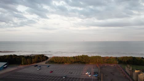 Luftaufnahmen-Zeigen-Eine-Atemberaubende-Strandszene-Bei-Sonnenuntergang-Mit-Nassem,-Glänzendem-Sand,-Einem-In-Lila--Und-Rosatönen-Bemalten-Meer-Und-Der-Silhouette-Von-Menschen,-Die-Mit-Ihrem-Hund-Spazieren-Gehen
