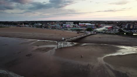 Aerial-video-captures-the-iconic-Skegness-pier-during-a-beautiful-sunset,-with-people-strolling-along-the-wooden-structure