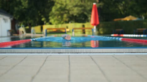 A-male-swimmer-swims-from-the-blur-into-the-focus-in-a-public-swimming-pool