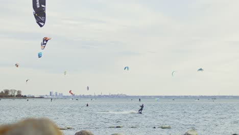 Kite-surfers-gliding-across-water-on-the-Nordic-coastline-of-Estonia,-backdropped-by-the-capital-city,-Tallinn