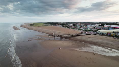 Sunset-paints-a-stunning-backdrop-for-Skegness-pier-in-this-aerial-footage,-capturing-people-as-they-walk-along-the-pier's-wooden-structure