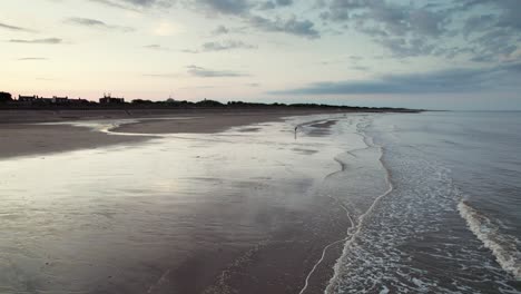 Das-Video-Von-Oben-Zeigt-Die-Pracht-Eines-Strandes-Bei-Sonnenuntergang-Mit-Glitzerndem,-Reflektierendem-Sand,-Einem-Ruhigen-Lila-rosafarbenen-Meer-Und-Menschen-Und-Ihrem-Hund-Als-Silhouette