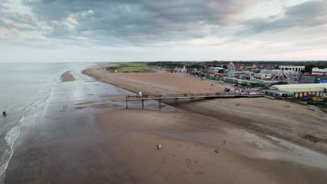 As-the-sun-sets,-Skegness-pier-takes-center-stage-in-this-aerial-video,-with-people-enjoying-a-tranquil-walk-along-the-wooden-pier