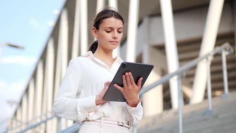 Young-businesswoman-stands-on-stairs-and-works-on-an-iPad-medium-shot