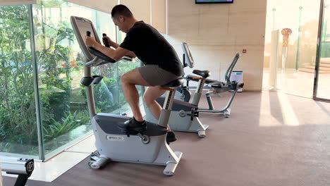 Young-Asian-Male-Pedalling-an-Exercise-Bike-in-an-Upscale-Luxurious-Gym