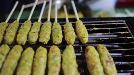 Nach-Unten-Geneigte-Aufnahme-Eines-Lebensmittelverkäufers,-Der-Gegrillten-Fischkuchen-Im-Thailändischen-Stil-Mit-Kräutern-Auf-Spießen-Auf-Einem-Heißen,-Flammenden-Holzkohlegrill-Zubereitet-Und-Kocht