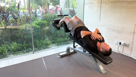 Young-Asian-man-doing-sit-ups-in-a-luxurious-high-end-gym-with-a-scenic-window-view