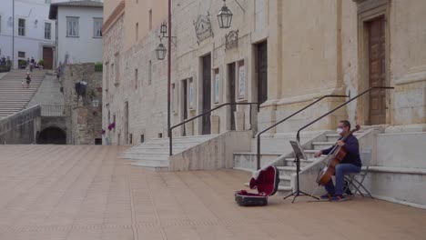 Ein-Musiker-Mit-Einer-Maske-Spielt-Cello-Oder-Violoncello-Auf-Dem-Berühmtesten-Platz-Von-Spoleto-In-Umbrien,-Der-„Piazza-Del-Duomo“-Genannt-Wird.