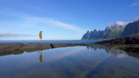 Tourist-walking-over-a-small-rocky-path,-enjoying-the-incredible-landscape-of-Senja,-reflecting-on-the-water-surface