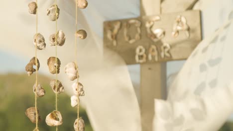 Cloth-waving-in-breeze-and-sea-shells-on-string-swaying-at-yoga-bar,-rack-focus