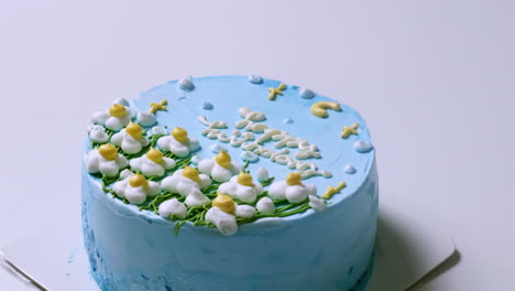 Zooming-in-on-a-birthday-cake-covered-with-blue-buttercream,-and-decorated-with-white-yellow-tipped-flowers