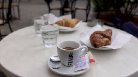 Woman-serving-an-Espresso-cup-on-a-terrace's-table-with-Italian-croissant
