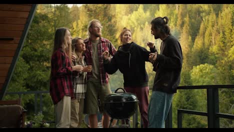 Warm-atmosphere-at-the-picnic:-the-guy-plays-the-guitar-and-his-friends-dance.-Entertainment-while-cooking-on-the-grill-against-the-background-of-mountains-and-coniferous-forest